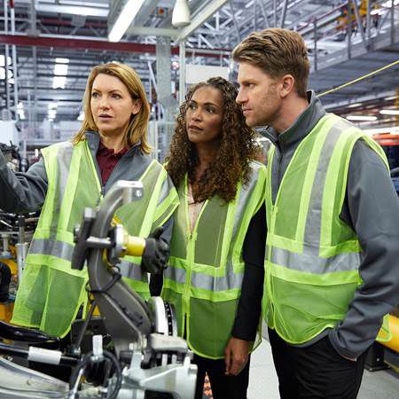 Gelijke Kansen Werving - Drie mensen in veiligheidsvesten observeren machines in een fabriek.